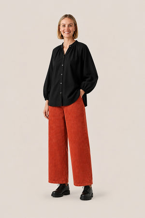 Pantalon en velours côtelé brique porté avec une chemise Arta unie noire